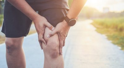 Injury from workout concept : Asian man use hands hold on his knee while running on road in the park. Shot in morning time, sunlight and warm effect with copy space for text or design Injury from workout concept : The asian man use hands hold on his knee while running on road in the park. Shot in morning time, sunlight and warm effect with copy space for text or design